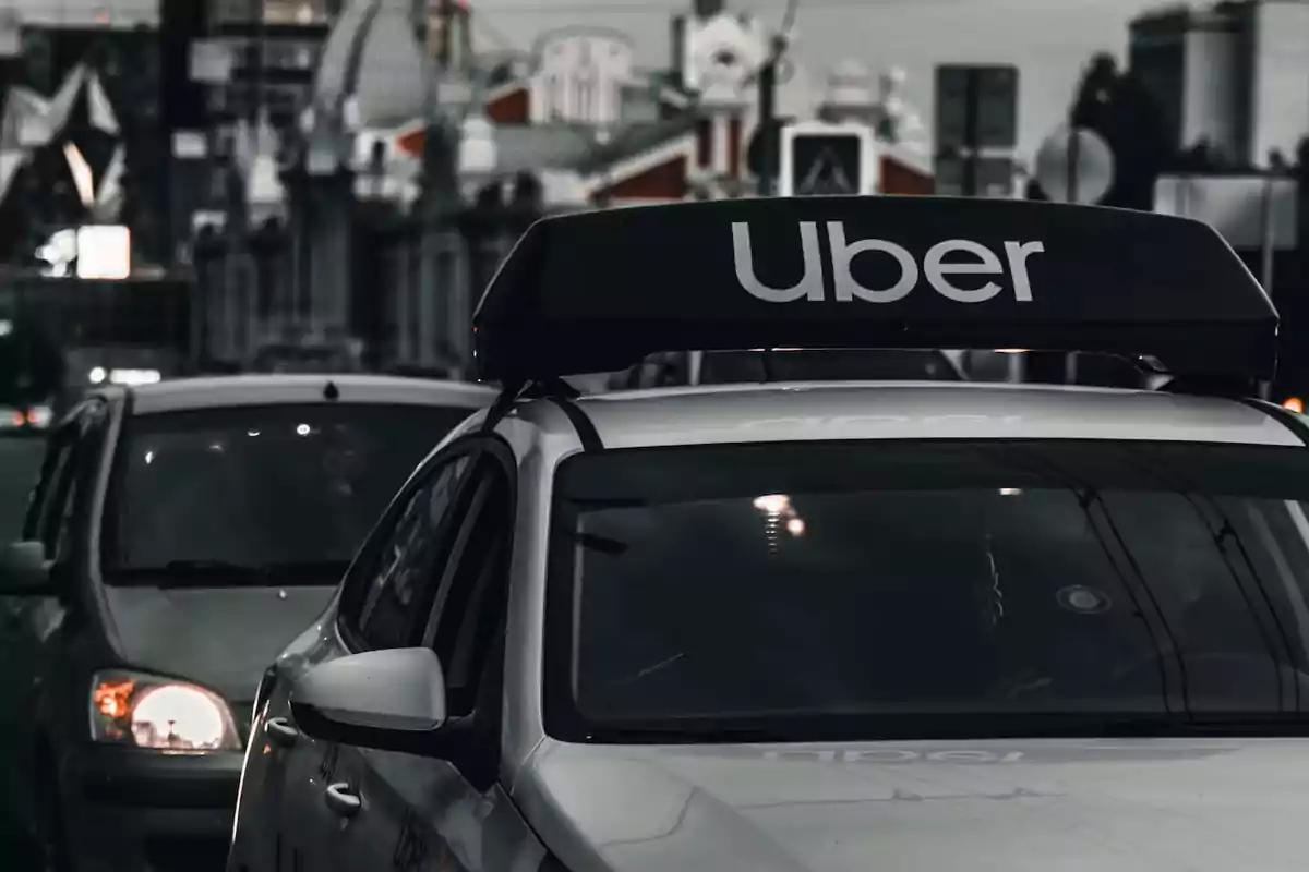 Auto blanco con letrero de Uber en el techo circulando por una ciudad al atardecer Auto blanco con letrero de Uber en el techo circulando por una ciudad al atardecer