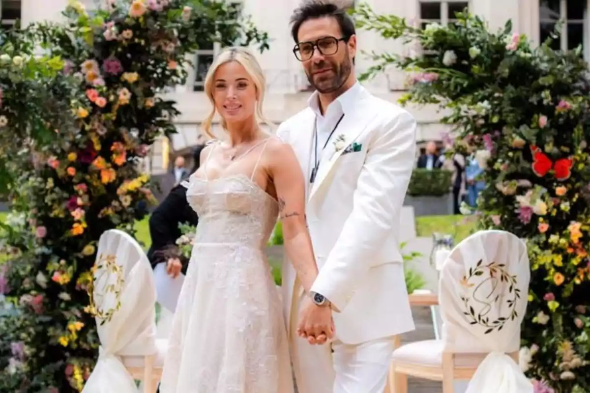 Newlywed couple posing together outdoors surrounded by floral arrangements and decorated chairs