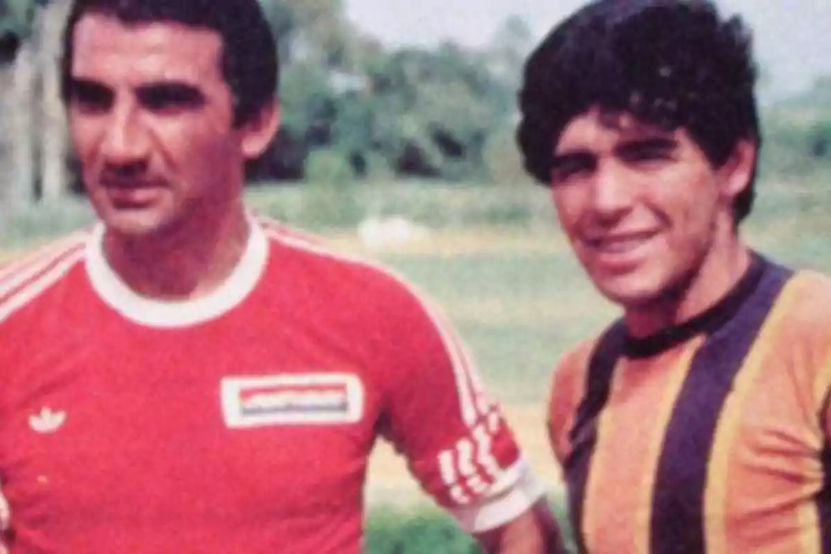 Two players pose together on a field; one is wearing a red jersey and the other a yellow jersey with black stripes. Two players pose together on a field; one is wearing a red jersey and the other a yellow jersey with black stripes.