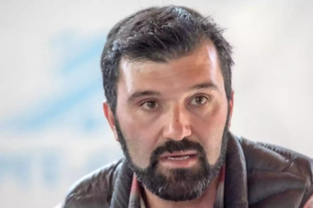 Dark-haired, bearded man in a quilted jacket looking straight ahead Dark-haired, bearded man in a quilted jacket looking straight ahead