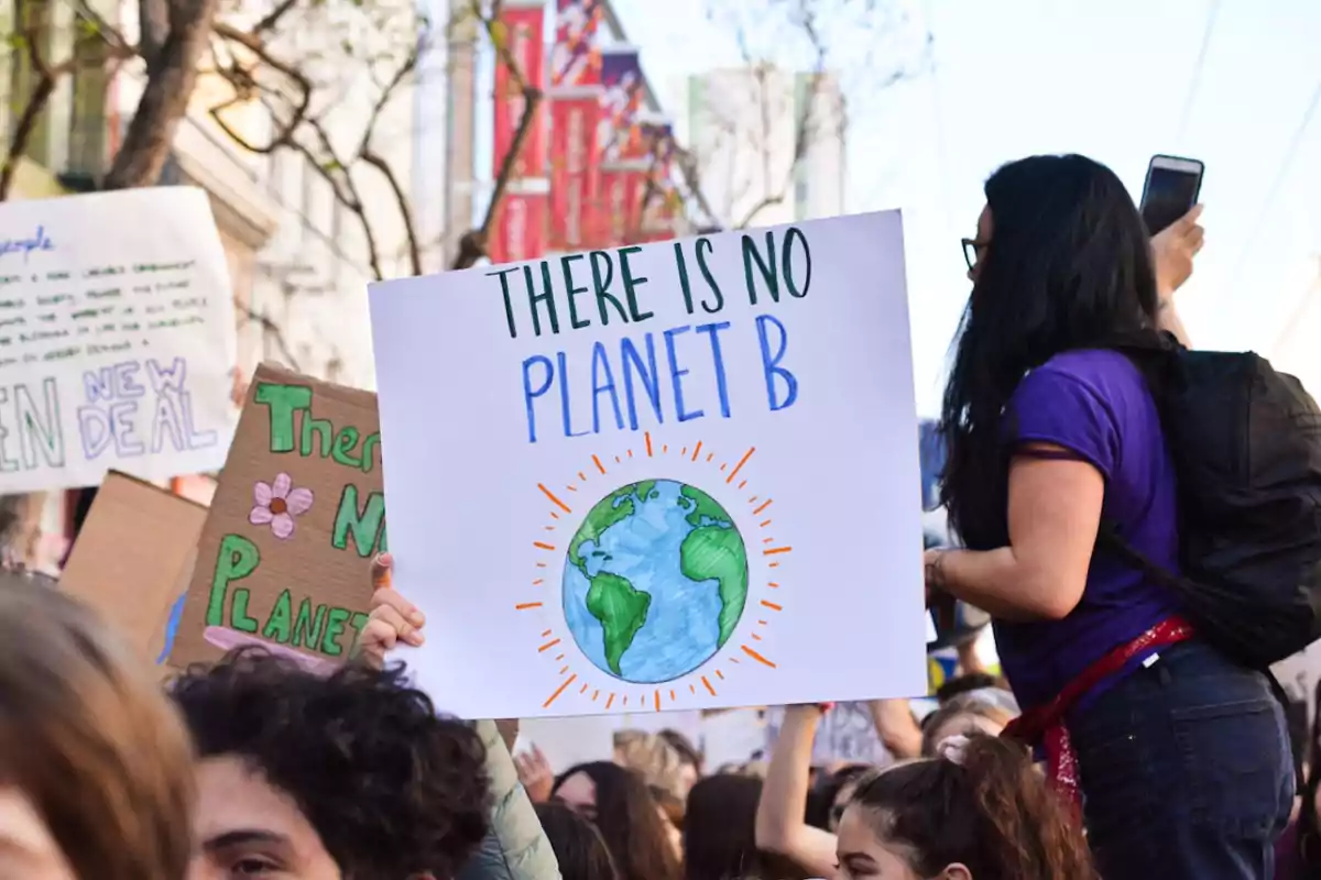 Personas manifestándose con carteles sobre el cambio climático, uno de ellos sostiene un letrero que dice There is no planet B acompañado de un dibujo del planeta Tierra Personas manifestándose con carteles sobre el cambio climático, uno de ellos sostiene un letrero que dice There is no planet B acompañado de un dibujo del planeta Tierra