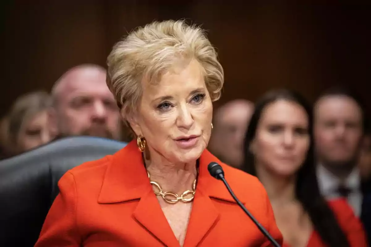 Blonde, short-haired woman speaking into a microphone with blurred people in the background Blonde, short-haired woman speaking into a microphone with blurred people in the background