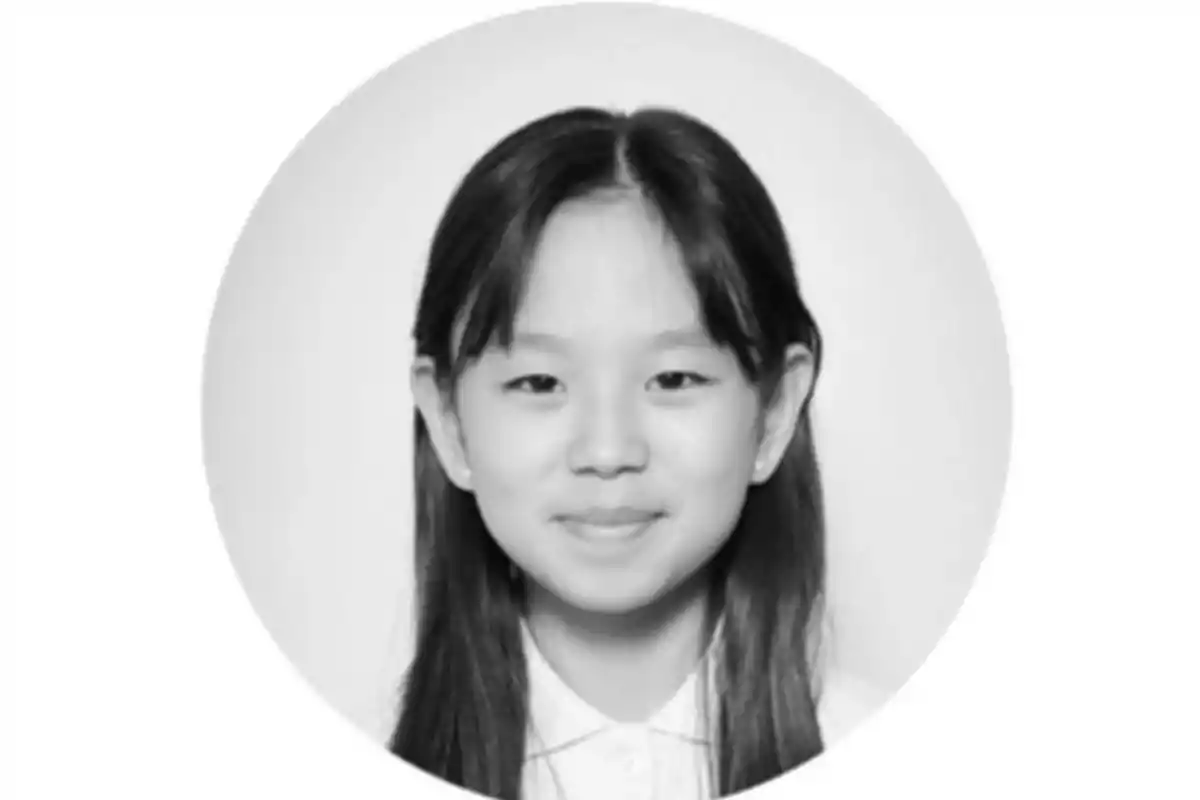 Retrato en blanco y negro de una niña joven con el cabello largo y lacio, sonriendo levemente frente a un fondo claro.