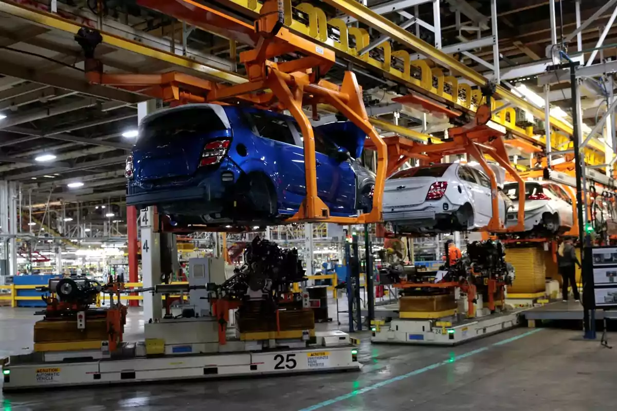 Línea de ensamblaje de automóviles en una fábrica con vehículos suspendidos y trabajadores en el fondo Línea de ensamblaje de automóviles en una fábrica con vehículos suspendidos y trabajadores en el fondo