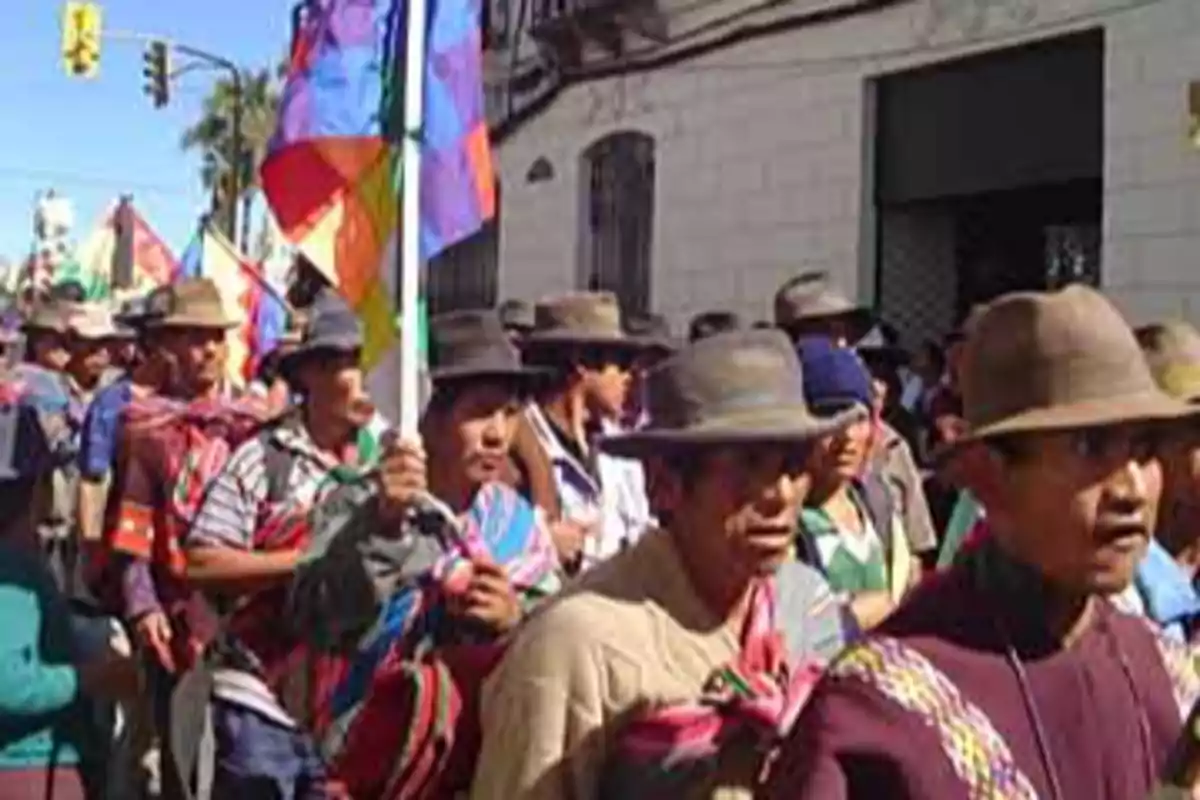 Group of Indigenous people marching down the street with multicolored flags and traditional clothing