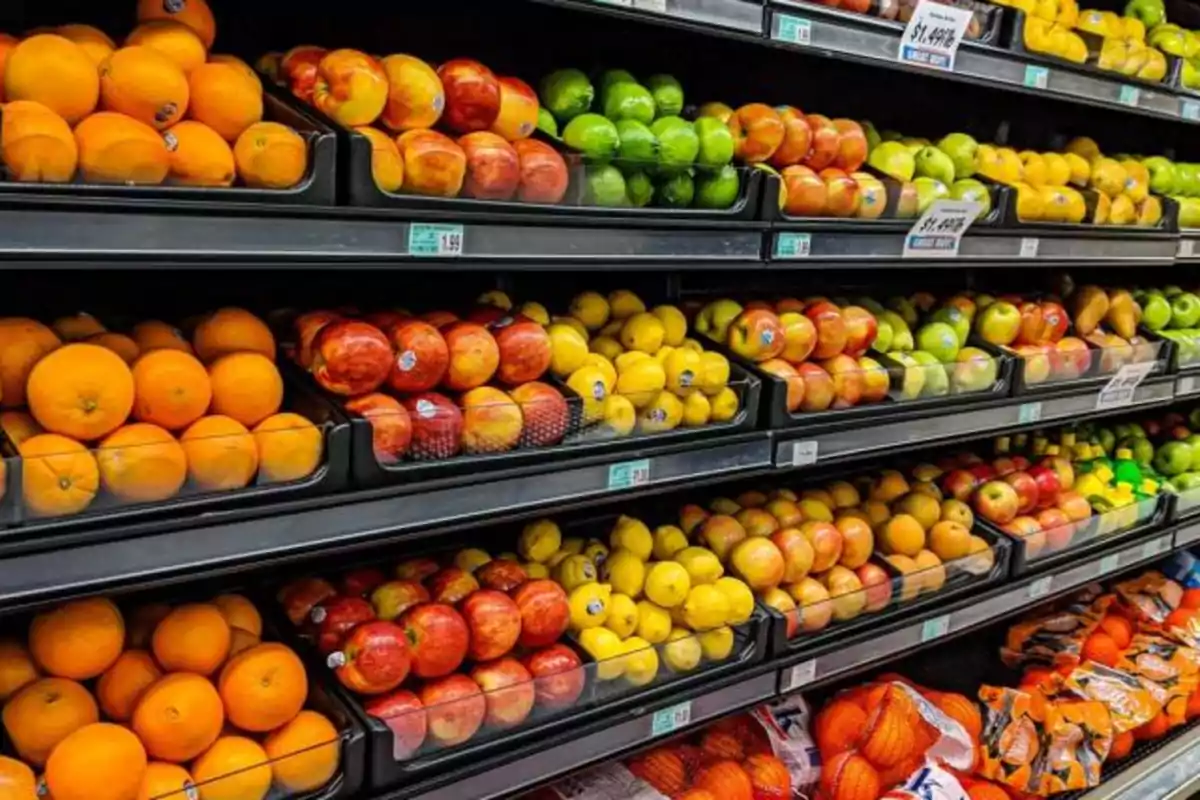 Estantes de supermercado llenos de frutas frescas como naranjas, manzanas, limones y manzanas verdes organizadas en filas