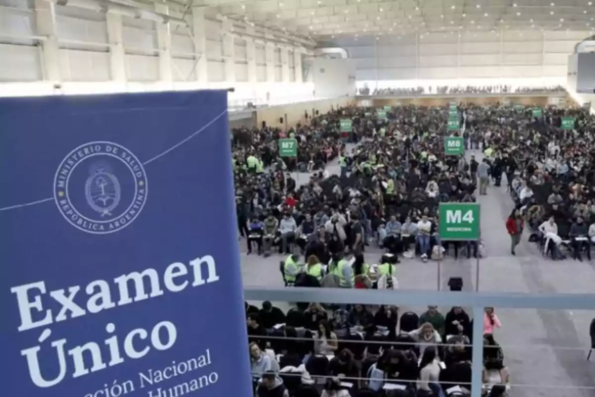 A large number of people sitting in a spacious hall taking a national health exam in Argentina, with green signs indicating different areas and a blue sign in the foreground that says Single Exam.