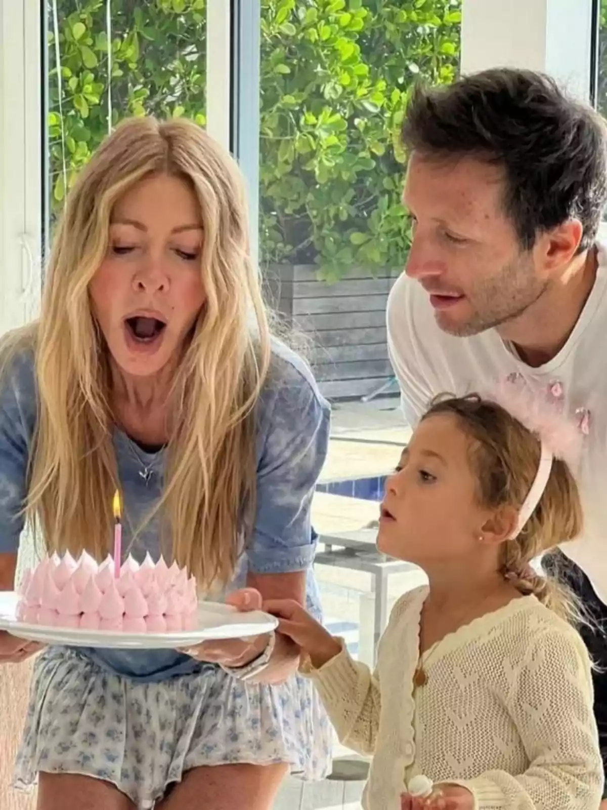 Tres personas celebran un cumpleaños mientras una mujer y una niña se preparan para soplar la vela de un pastel rosa Tres personas celebran un cumpleaños mientras una mujer y una niña se preparan para soplar la vela de un pastel rosa