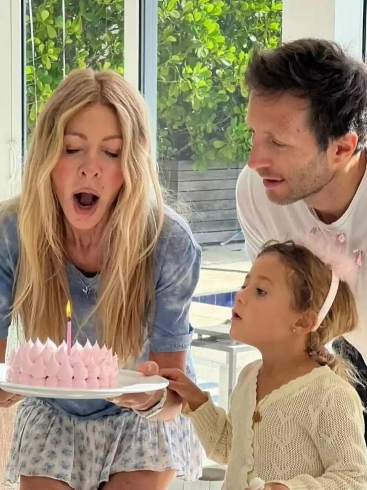 Tres personas soplan una vela encendida sobre un pastel rosa en una celebración de cumpleaños Tres personas soplan una vela encendida sobre un pastel rosa en una celebración de cumpleaños