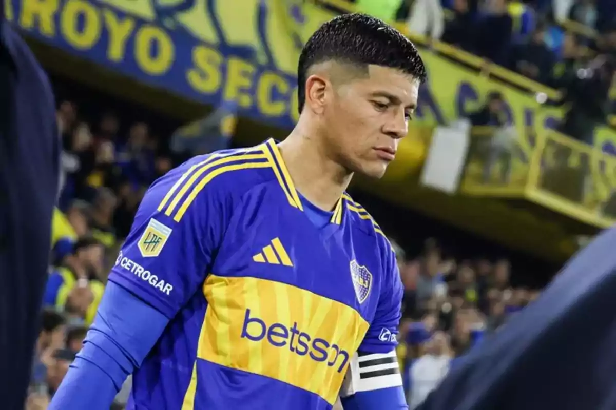 Jugador de fútbol con camiseta azul y amarilla de Boca Juniors y brazalete de capitán en un estadio lleno de aficionados Jugador de fútbol con camiseta azul y amarilla de Boca Juniors y brazalete de capitán en un estadio lleno de aficionados