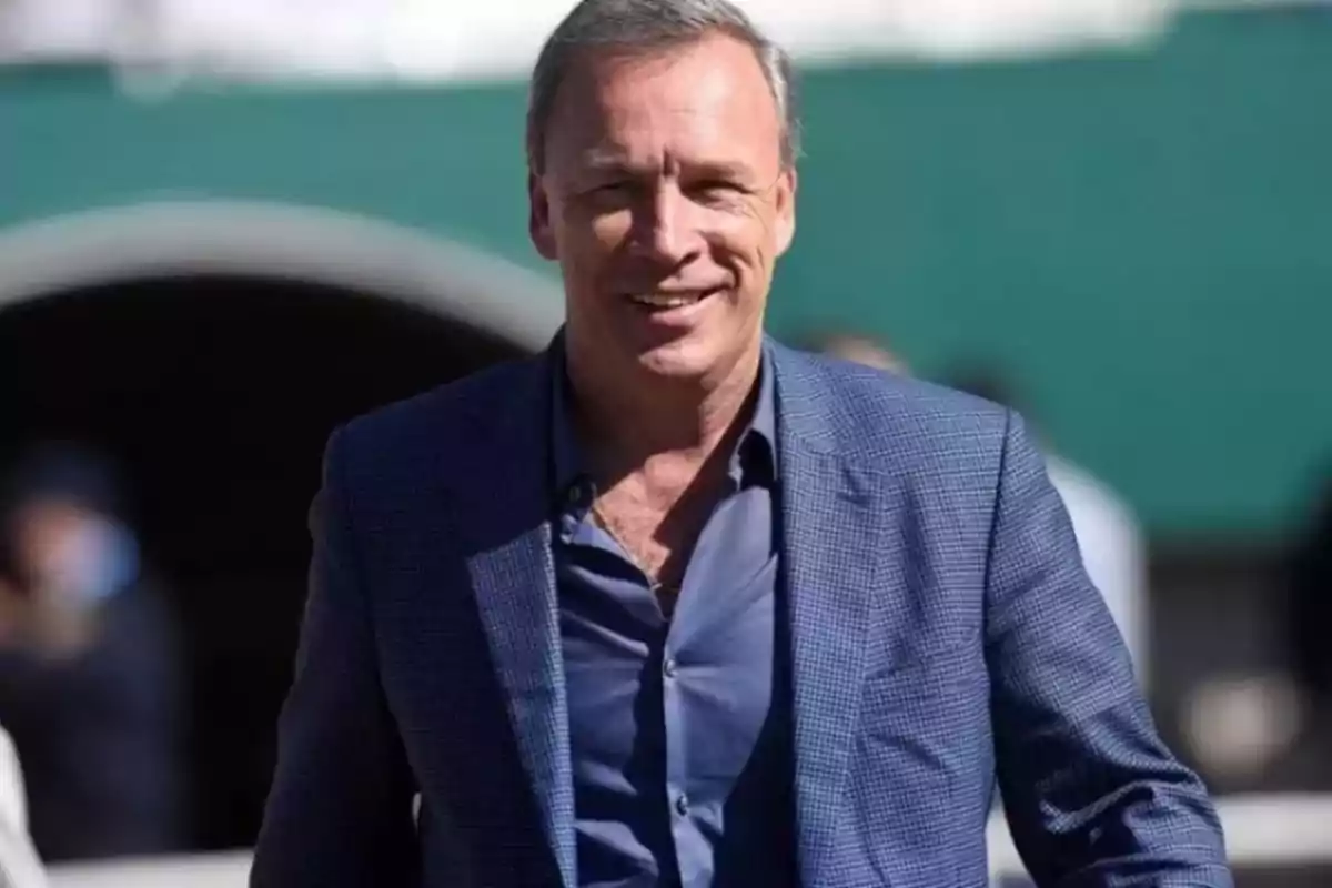 Hombre de cabello canoso con saco azul y camisa azul oscuro sonriendo al aire libre Hombre de cabello canoso con saco azul y camisa azul oscuro sonriendo al aire libre