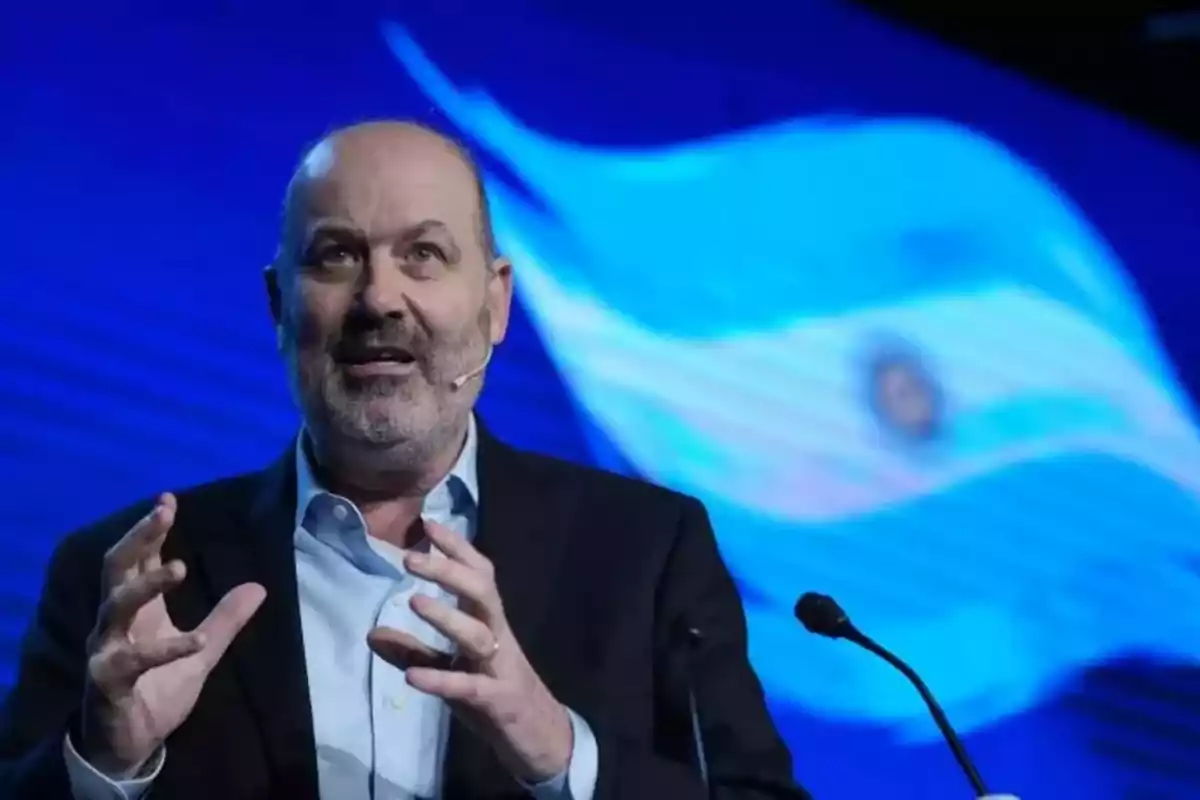 Bald man with a beard speaking on a stage with a headset microphone and a blurred Argentine flag in the background Bald man with a beard speaking on a stage with a headset microphone and a blurred Argentine flag in the background