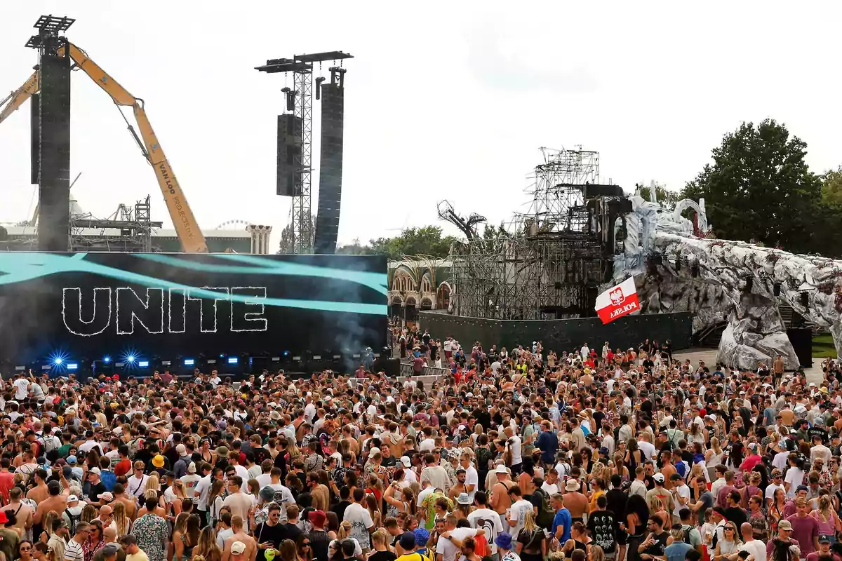 Multitud de personas reunidas frente a un escenario al aire libre con la palabra UNITE en una pantalla gigante y estructuras de escenografía a los lados