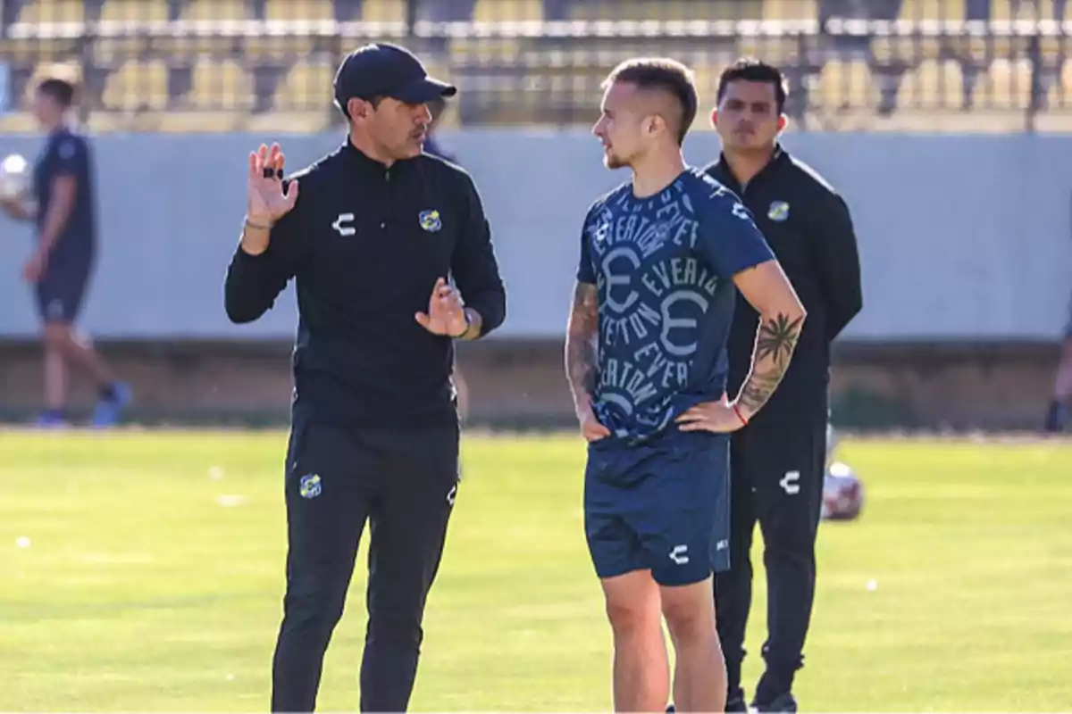 Coach and player talking on a soccer field during a training session while another person watches in the background Coach and player talking on a soccer field during a training session while another person watches in the background
