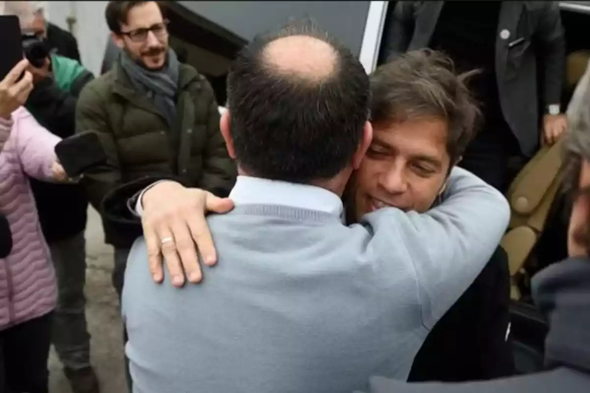 Dos hombres se abrazan mientras varias personas alrededor los observan y toman fotos