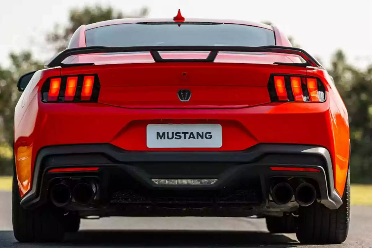 Vista trasera de un auto deportivo Ford Mustang rojo con luces traseras encendidas y doble escape Vista trasera de un auto deportivo Ford Mustang rojo con luces traseras encendidas y doble escape
