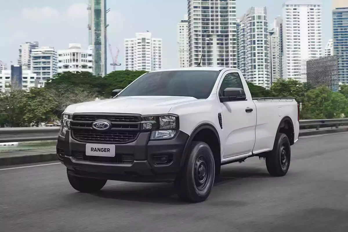 Camioneta Ford Ranger blanca de cabina sencilla circulando por una avenida con edificios altos al fondo Camioneta Ford Ranger blanca de cabina sencilla circulando por una avenida con edificios altos al fondo