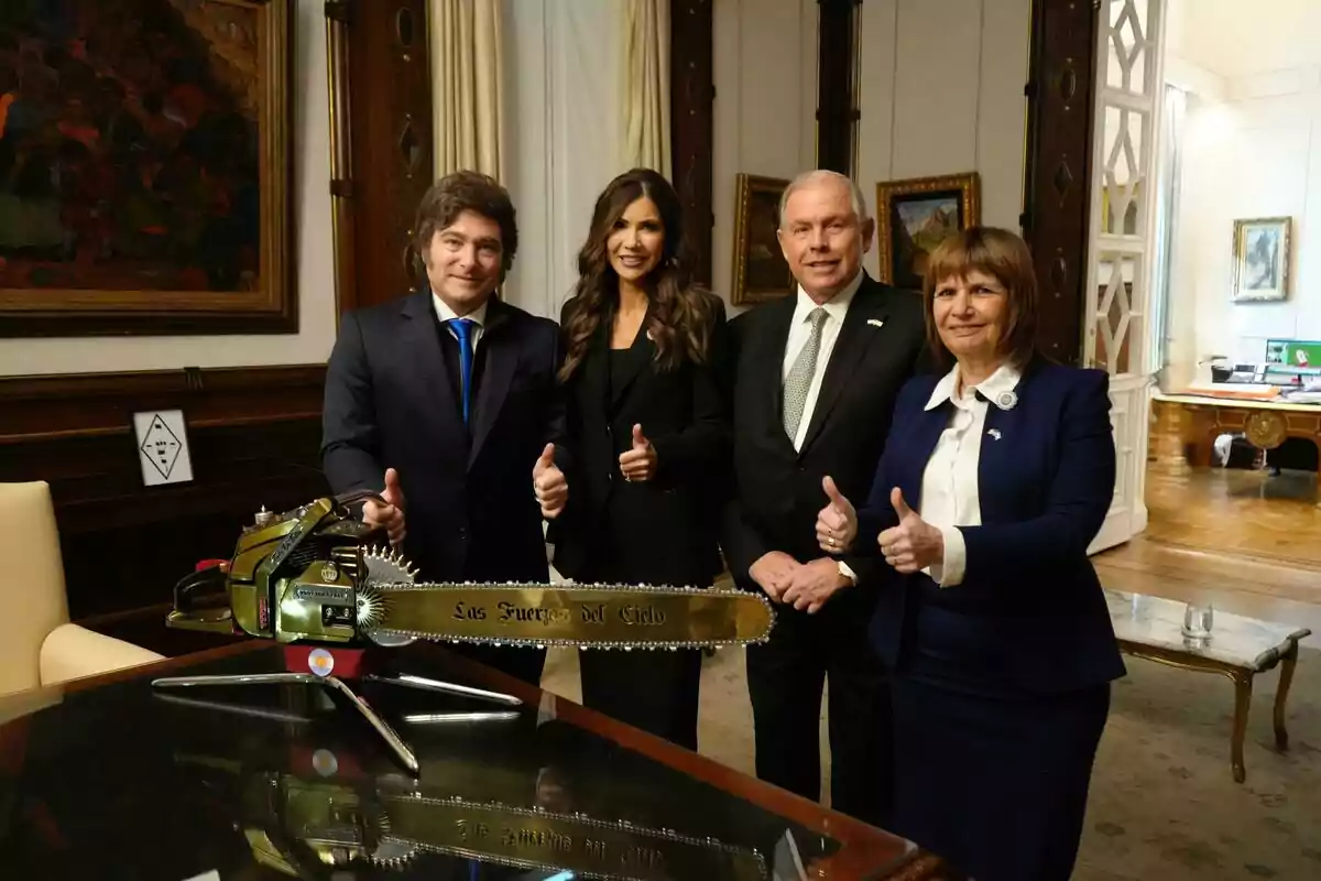 Cuatro personas posan sonrientes con pulgares arriba junto a una motosierra dorada sobre una mesa en una oficina elegante Cuatro personas posan sonrientes con pulgares arriba junto a una motosierra dorada sobre una mesa en una oficina elegante