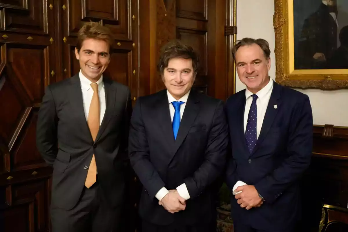Tres hombres vestidos con traje posan sonrientes en una sala elegante con paredes de madera y un cuadro antiguo al fondo Tres hombres vestidos con traje posan sonrientes en una sala elegante con paredes de madera y un cuadro antiguo al fondo