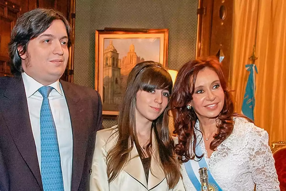 Three people pose together in a formal setting with an Argentine flag and a painting in the background. Three people pose together in a formal setting with an Argentine flag and a painting in the background.