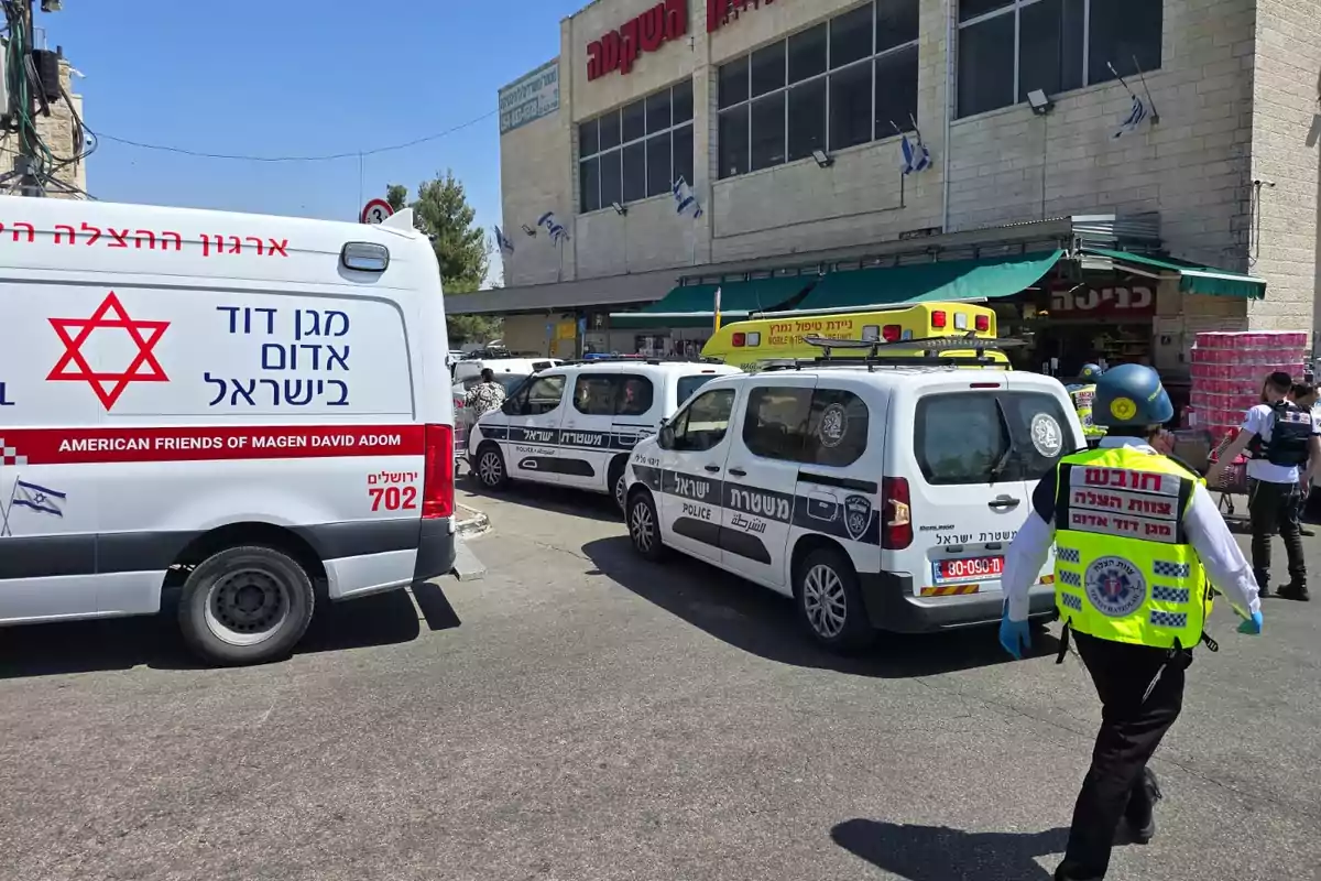 Several emergency and police vehicles are parked in front of a building, while medical and security personnel walk around the scene.