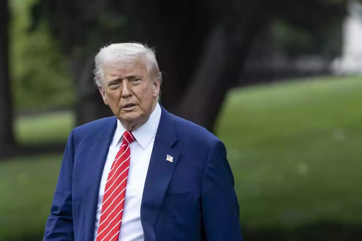 Gray-haired man in a blue suit and red tie walking outdoors in a green setting
