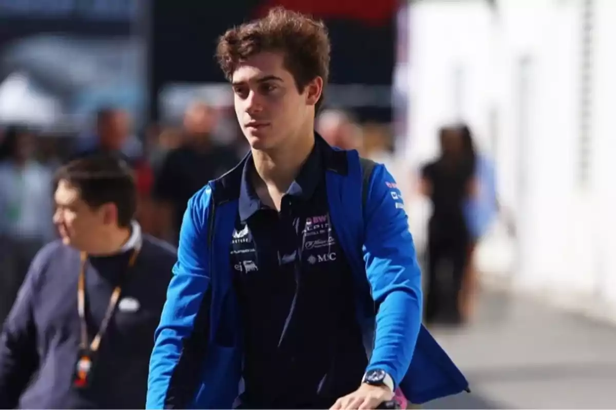 Young man in a blue jacket and dark t-jersey walks in an urban setting with blurred people in the background