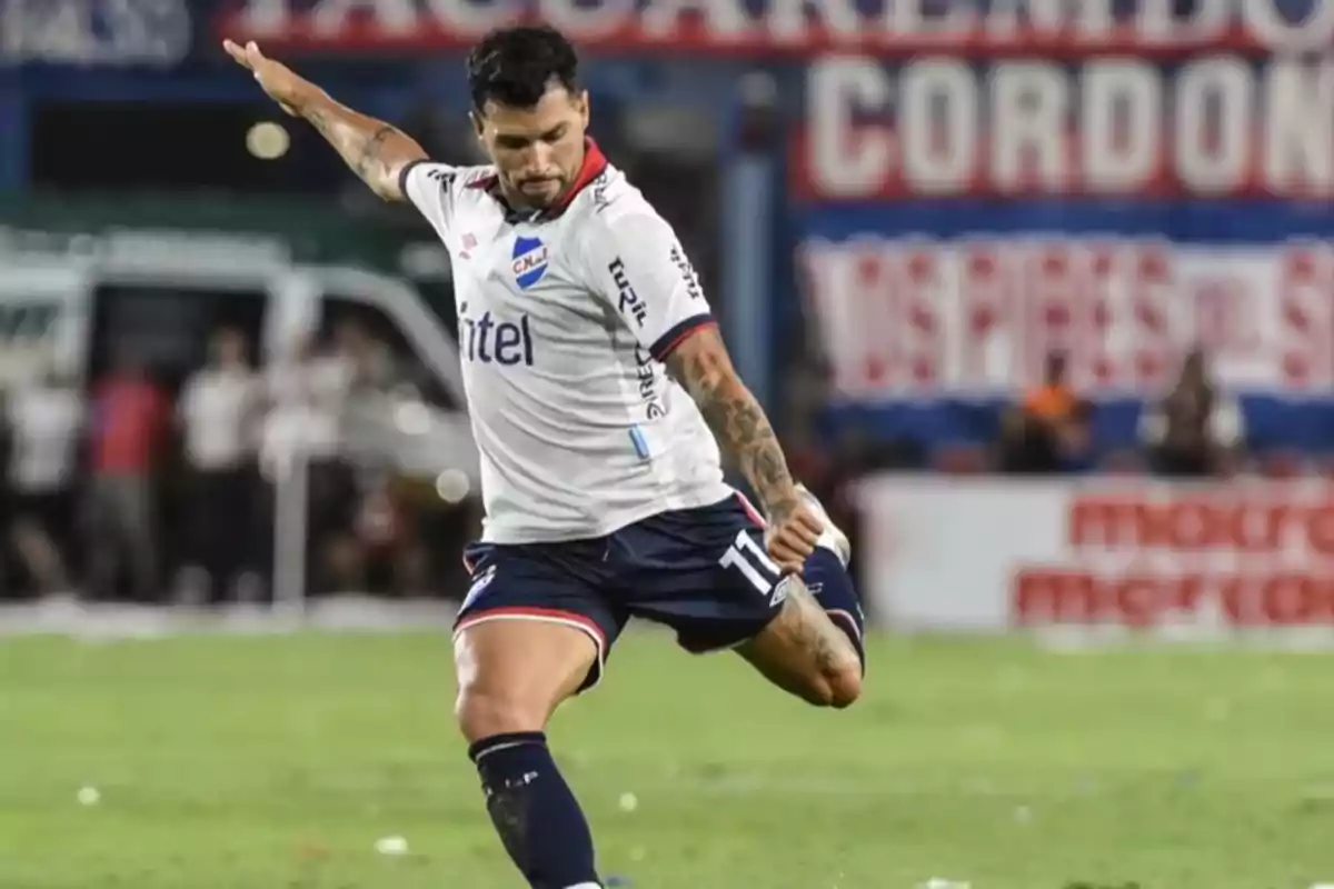 Soccer player in a white and blue uniform kicking a ball in a stadium during a match