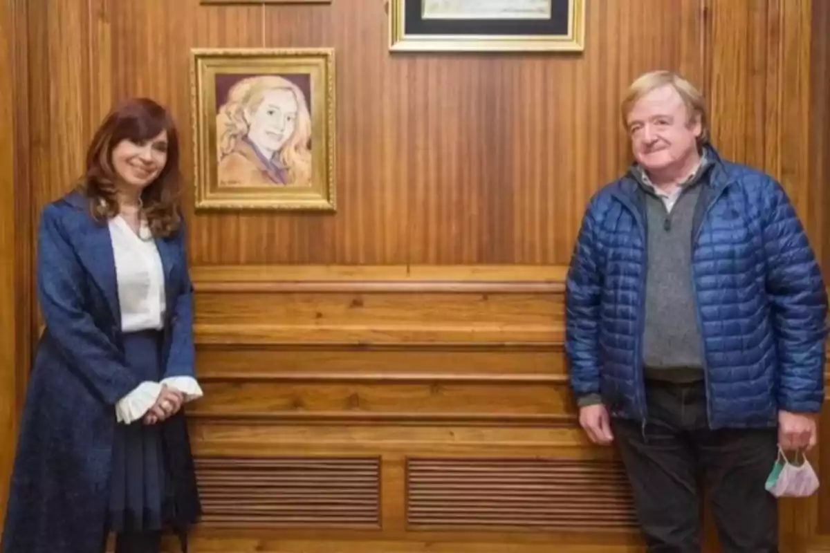 Dos personas posan sonriendo en una habitación de madera junto a un retrato enmarcado de una mujer rubia Dos personas posan sonriendo en una habitación de madera junto a un retrato enmarcado de una mujer rubia