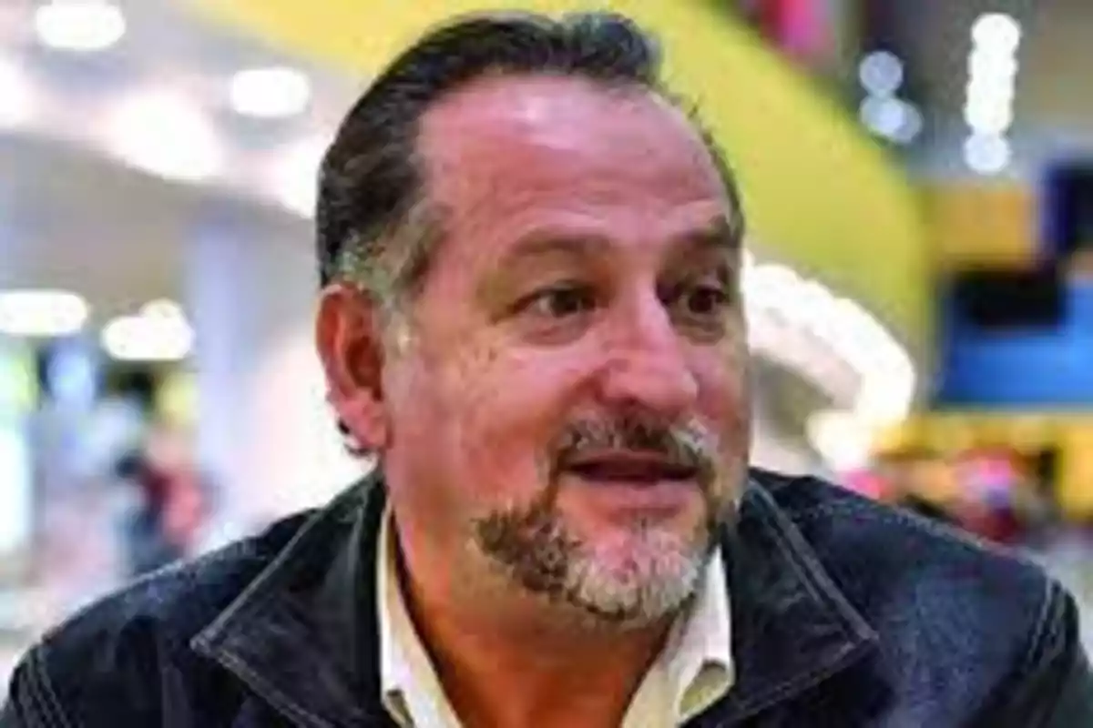 Middle-aged man with a beard and mustache, wearing a dark jacket and a light jersey, in a well-lit indoor setting Middle-aged man with a beard and mustache, wearing a dark jacket and a light jersey, in a well-lit indoor setting