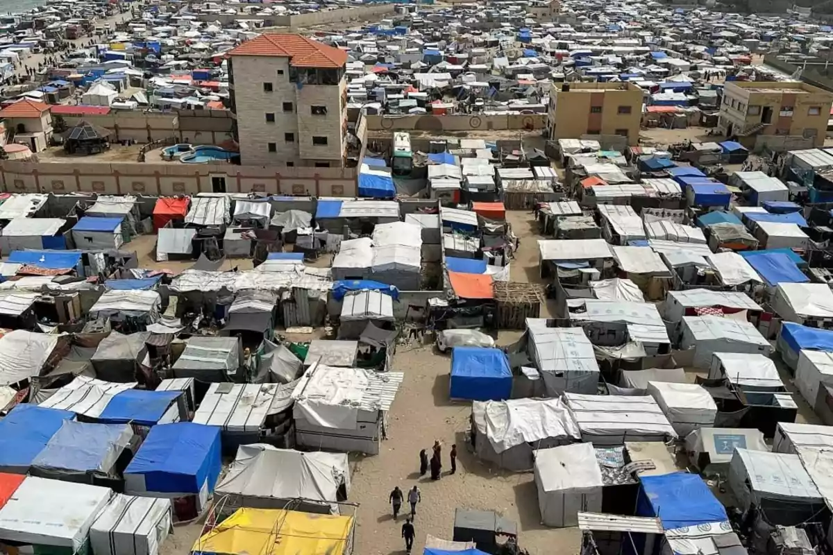 Vista aérea de un campamento de refugiados con numerosas tiendas improvisadas de diferentes colores y algunas personas caminando entre ellas Vista aérea de un campamento de refugiados con numerosas tiendas improvisadas de diferentes colores y algunas personas caminando entre ellas
