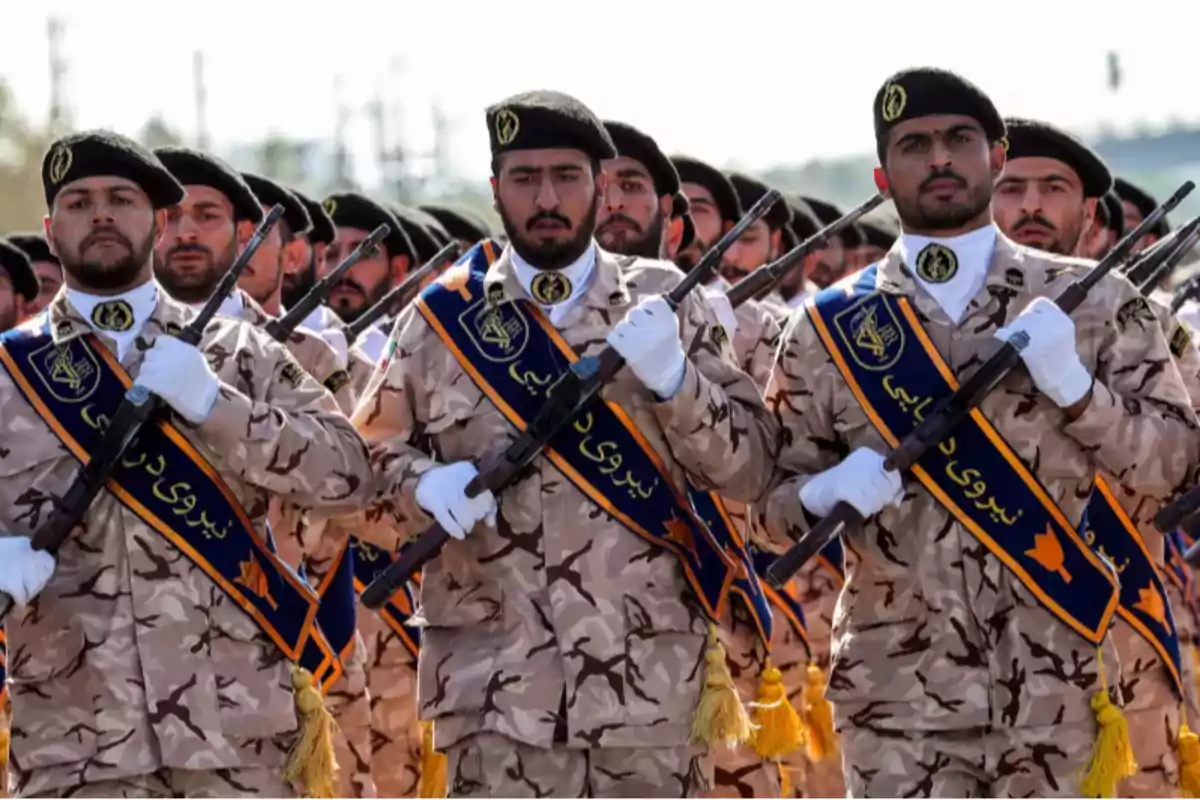 Uniformed soldiers march in formation holding rifles and wearing black berets.