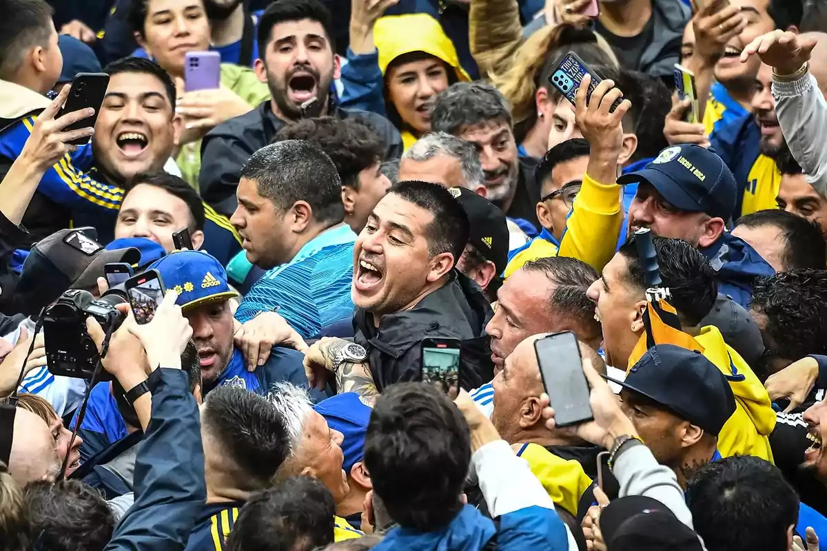 Un grupo de aficionados celebra con entusiasmo rodeando a una persona sonriente en el centro mientras muchos levantan sus teléfonos para tomar fotos Un grupo de aficionados celebra con entusiasmo rodeando a una persona sonriente en el centro mientras muchos levantan sus teléfonos para tomar fotos
