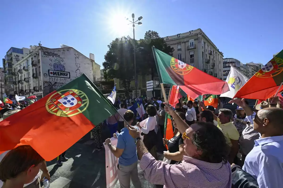 People protesting in the street waving Portuguese flags under a sunny sky in a European city People protesting in the street waving Portuguese flags under a sunny sky in a European city