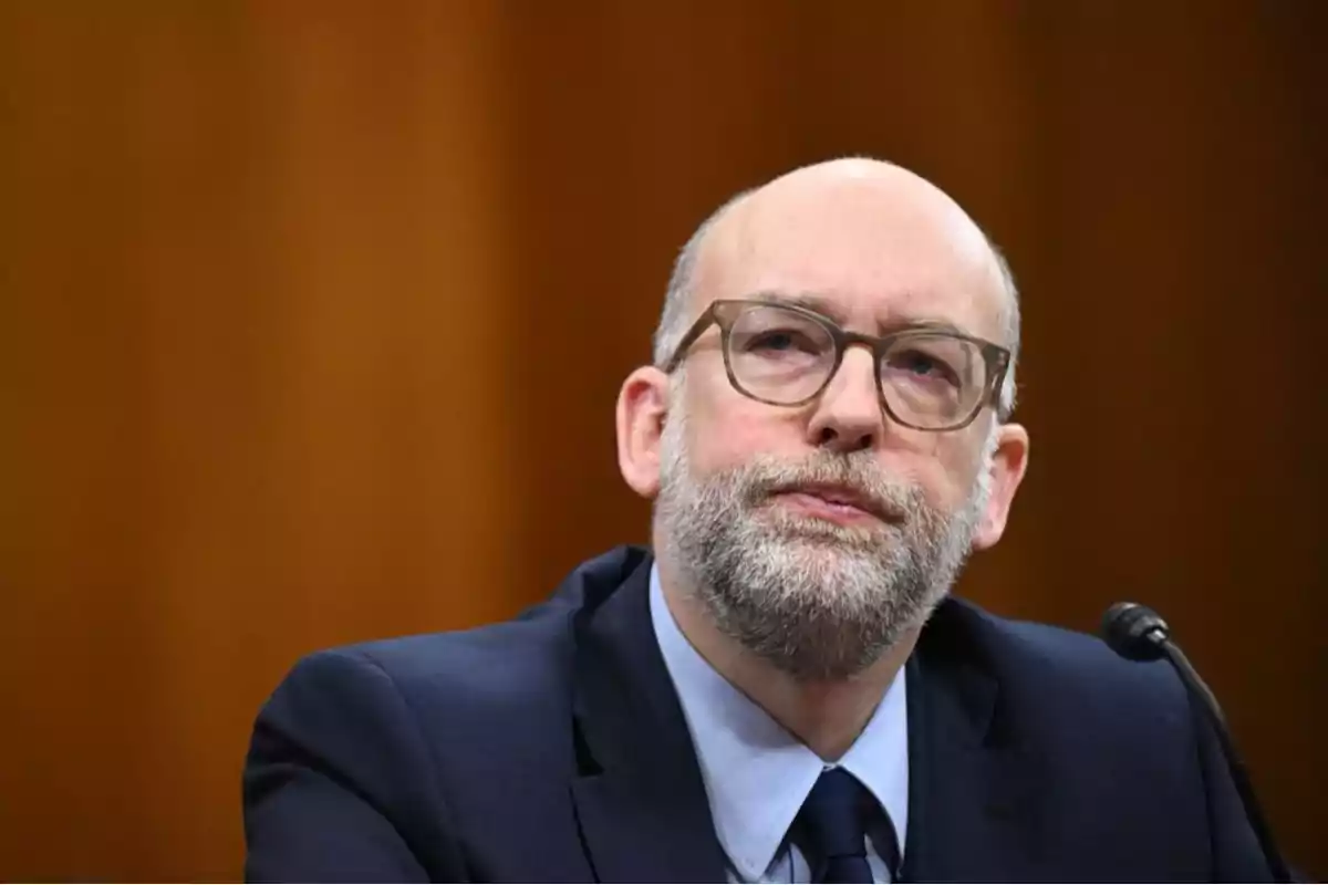 Middle-aged man with a beard and glasses sitting in front of a microphone with a brown background Middle-aged man with a beard and glasses sitting in front of a microphone with a brown background