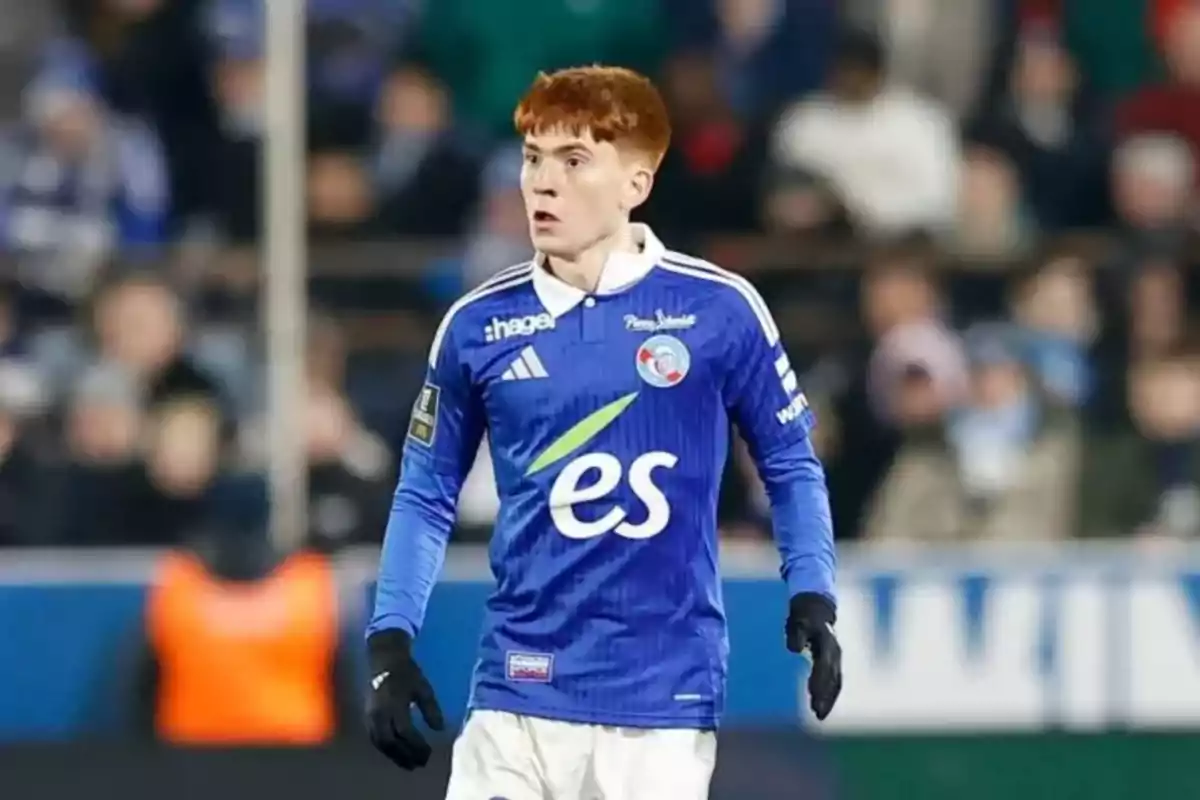 Futbolista con cabello corto y rojizo usando uniforme azul con detalles blancos en un estadio durante un partido Futbolista con cabello corto y rojizo usando uniforme azul con detalles blancos en un estadio durante un partido