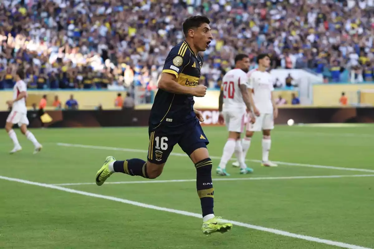 Futbolista con uniforme azul y amarillo celebrando un gol en un estadio lleno de aficionados mientras jugadores rivales observan al fondo Futbolista con uniforme azul y amarillo celebrando un gol en un estadio lleno de aficionados mientras jugadores rivales observan al fondo