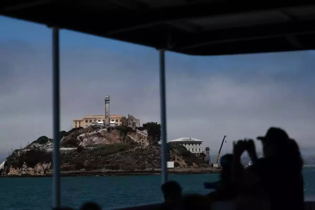 Vista de la isla de Alcatraz desde un barco con una persona en primer plano tomando una foto Vista de la isla de Alcatraz desde un barco con una persona en primer plano tomando una foto