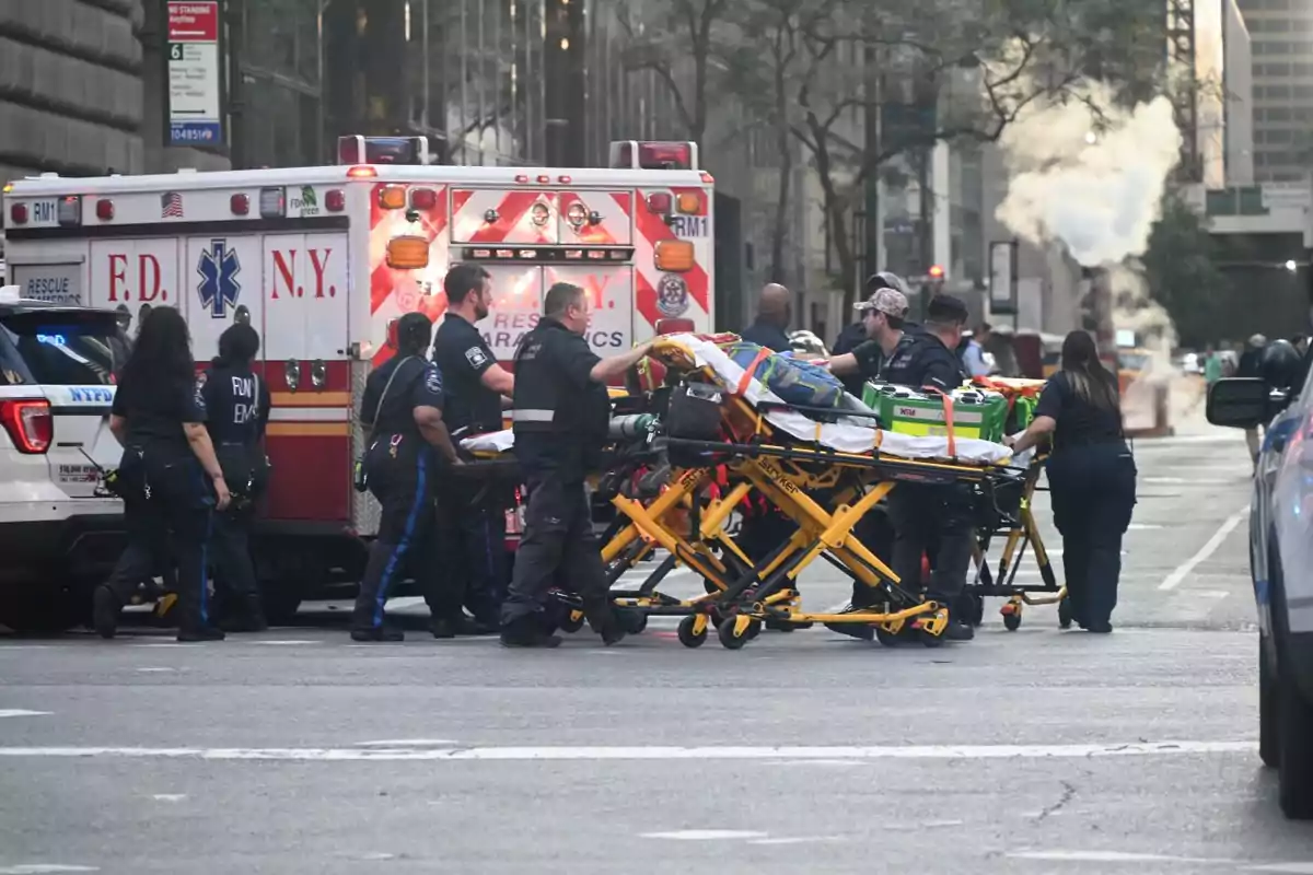 Paramédicos y personal de emergencia atienden una situación en la calle junto a una ambulancia y camillas en una ciudad