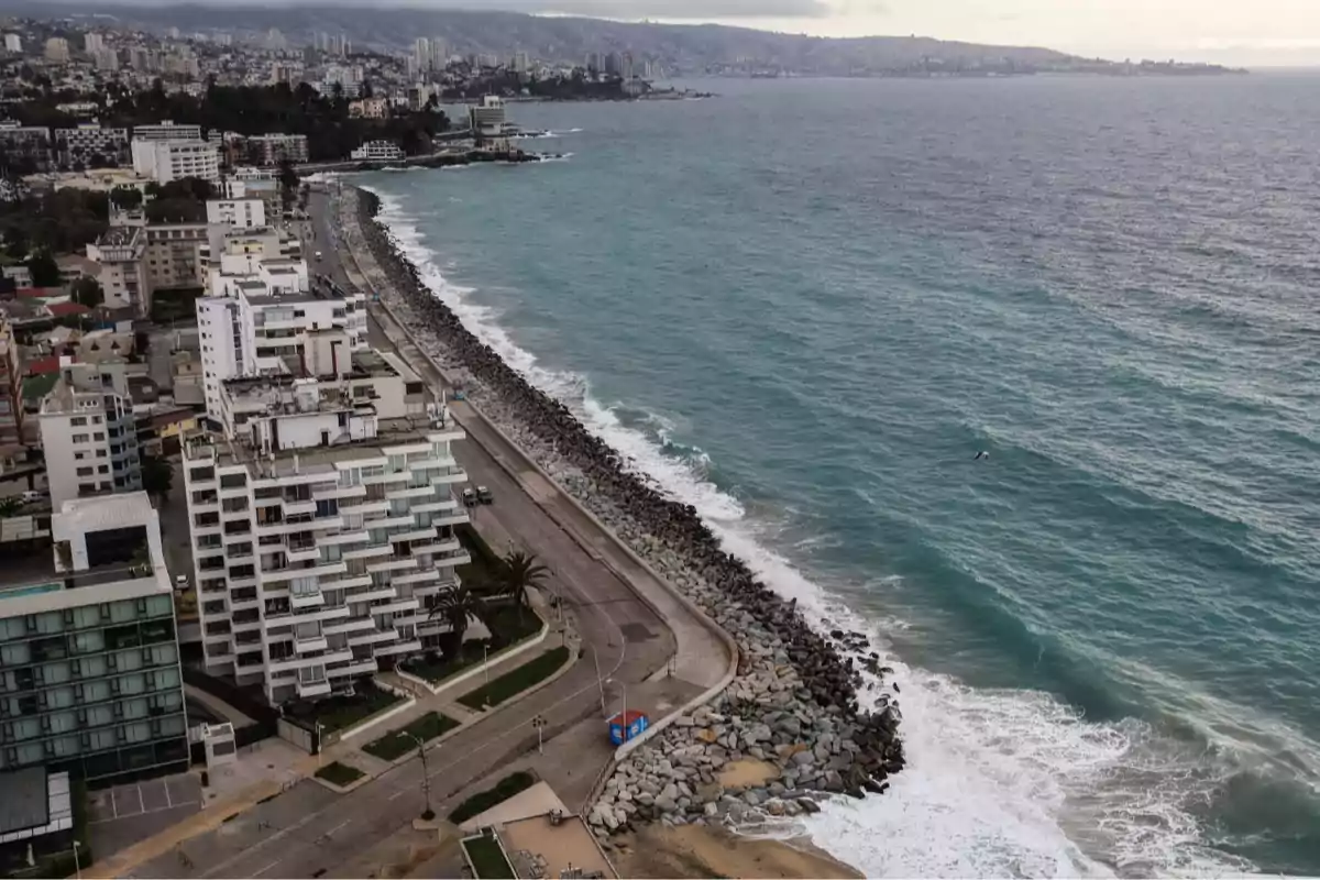 Aerial view of a coastal city with buildings by the sea and a seawall protected by rocks, with waves breaking on the shore and an urban landscape in the background Aerial view of a coastal city with buildings by the sea and a seawall protected by rocks, with waves breaking on the shore and an urban landscape in the background