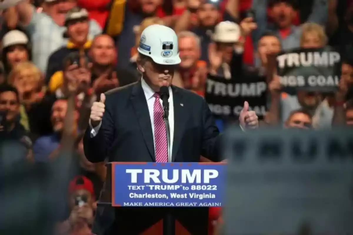 Donald Trump wearing a safety helmet at a rally surrounded by supporters with banners and signs of support