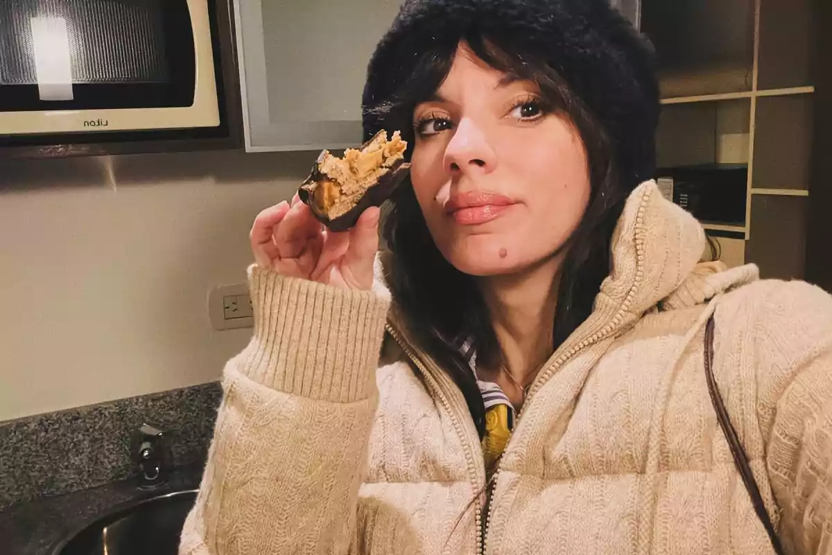 Woman in a beige coat and dark hat holds a piece of bread with peanut butter in a kitchen Woman in a beige coat and dark hat holds a piece of bread with peanut butter in a kitchen