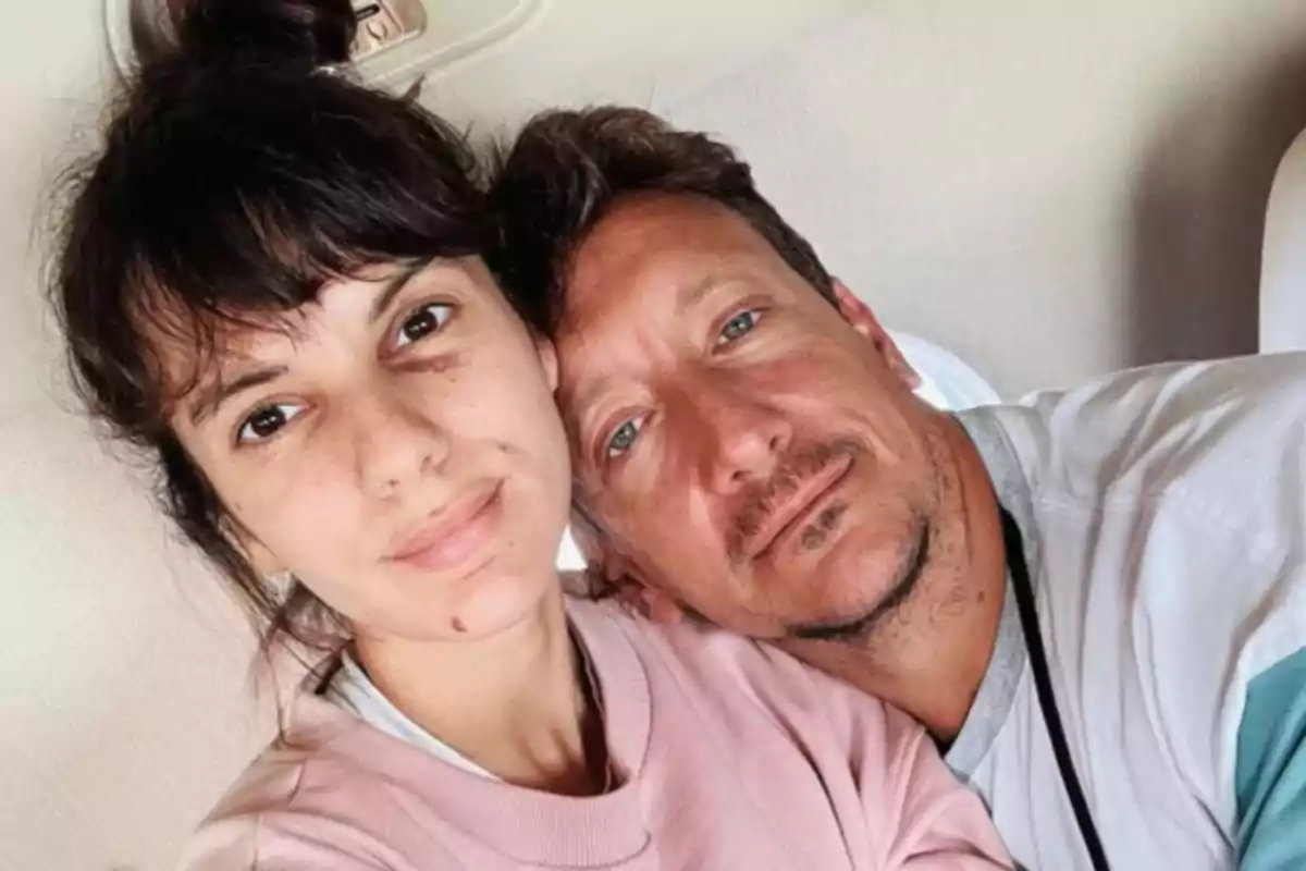 Couple hugging, sitting on a sofa, looking at the camera with relaxed expressions