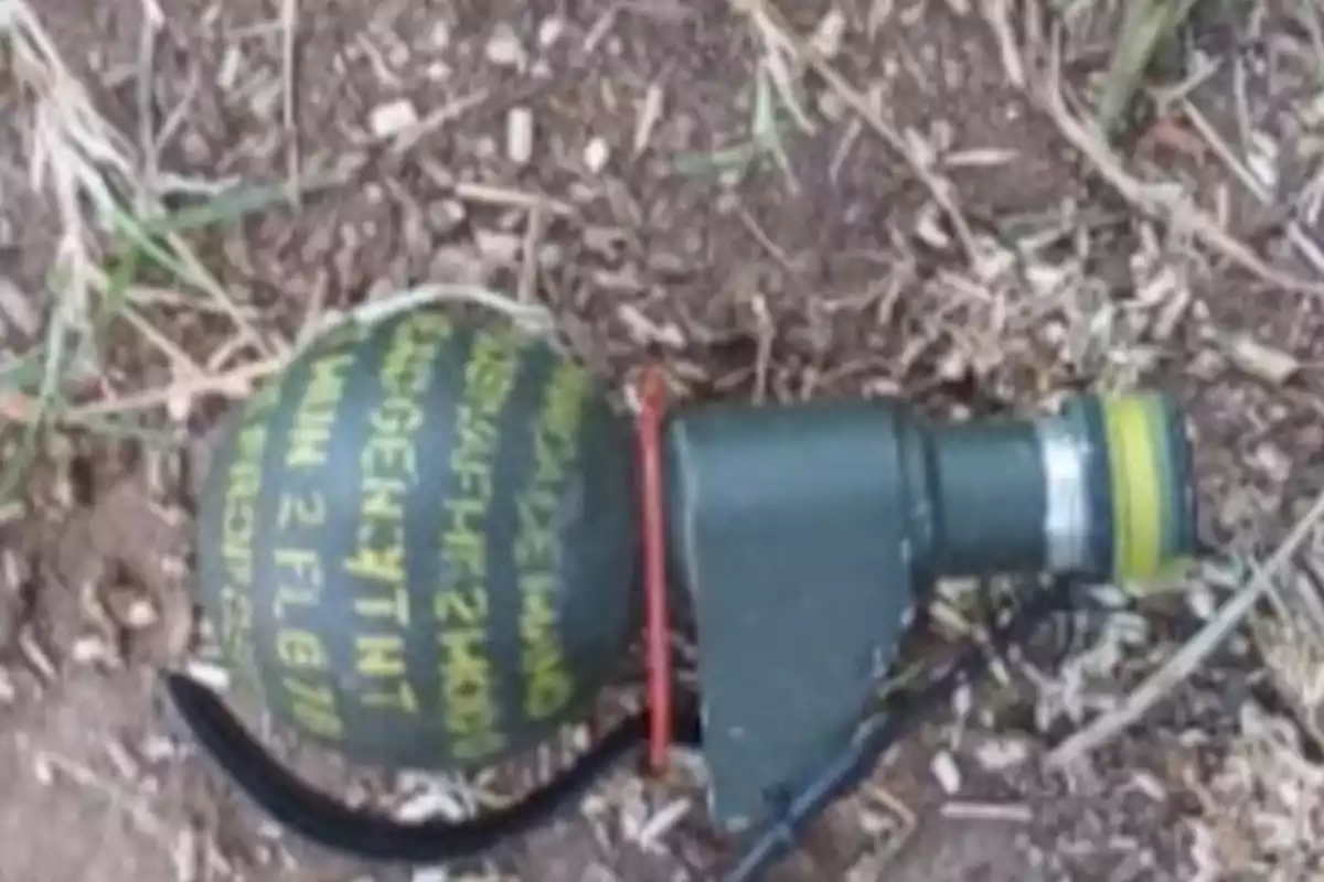 Green hand grenade with yellow inscriptions on dirt and dry grass