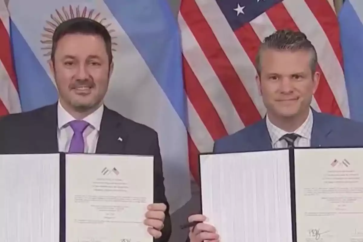 Dos hombres de traje sonríen mientras sostienen documentos frente a las banderas de Argentina y Estados Unidos Dos hombres de traje sonríen mientras sostienen documentos frente a las banderas de Argentina y Estados Unidos