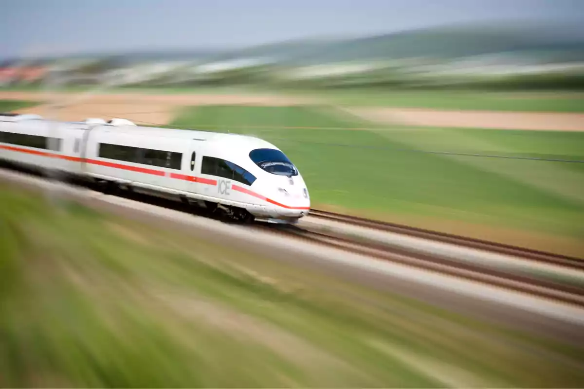 Tren de alta velocidad blanco avanzando rápidamente por vías en un paisaje rural desenfocado Tren de alta velocidad blanco avanzando rápidamente por vías en un paisaje rural desenfocado