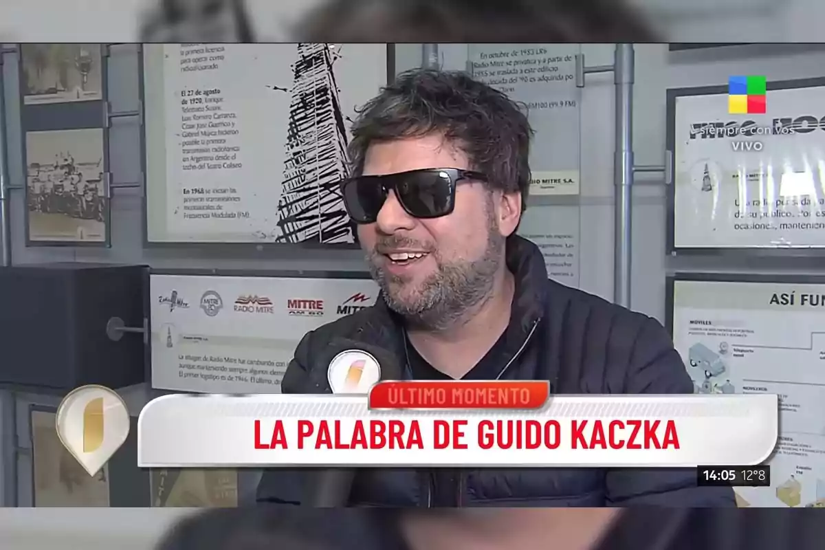 A man with sunglasses and a beard is being interviewed in a radio studio, with an on-screen graphic that says A man with sunglasses and a beard is being interviewed in a radio studio, with an on-screen graphic that says