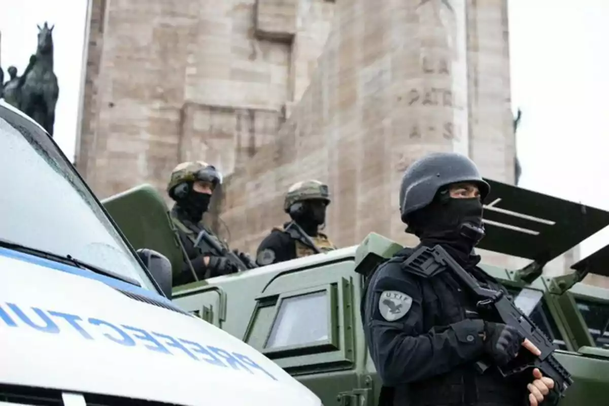 Policías fuertemente armados con equipo táctico y vehículos blindados en una operación de seguridad frente a un monumento de piedra.