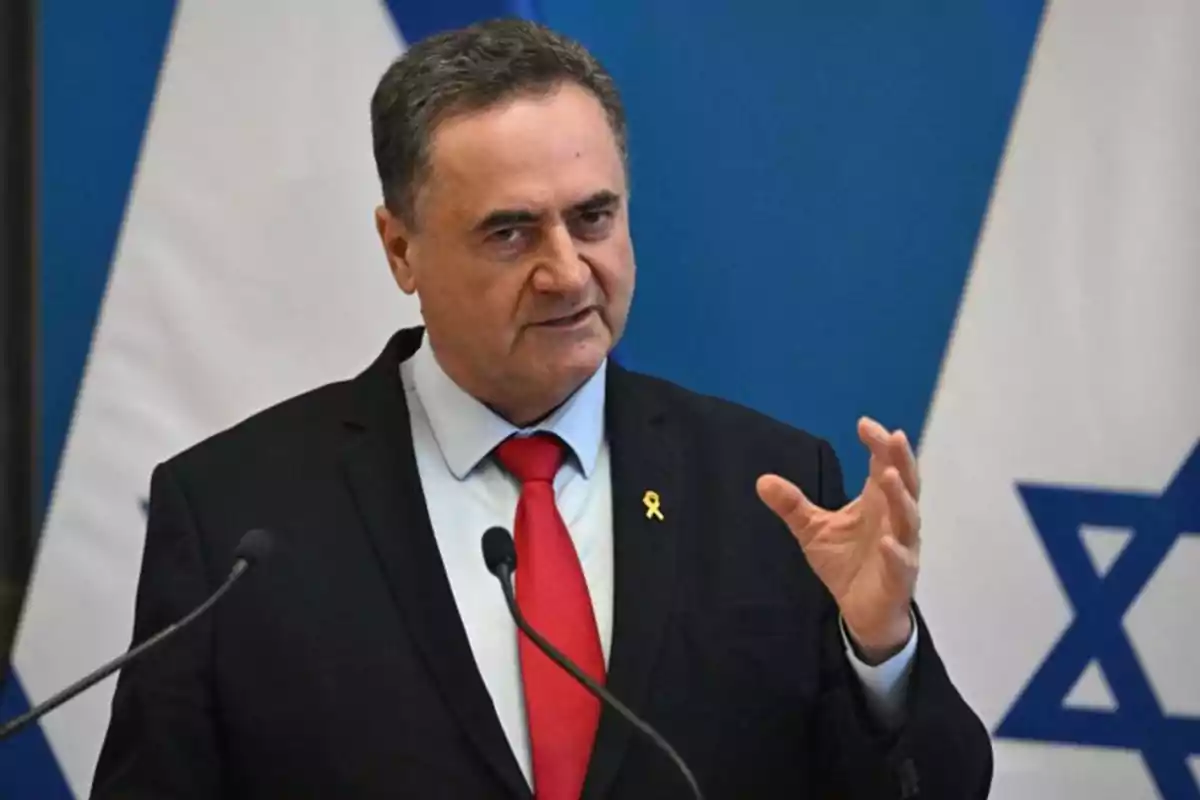 Hombre de traje oscuro y corbata roja hablando frente a micrófonos con banderas de Israel al fondo Hombre de traje oscuro y corbata roja hablando frente a micrófonos con banderas de Israel al fondo
