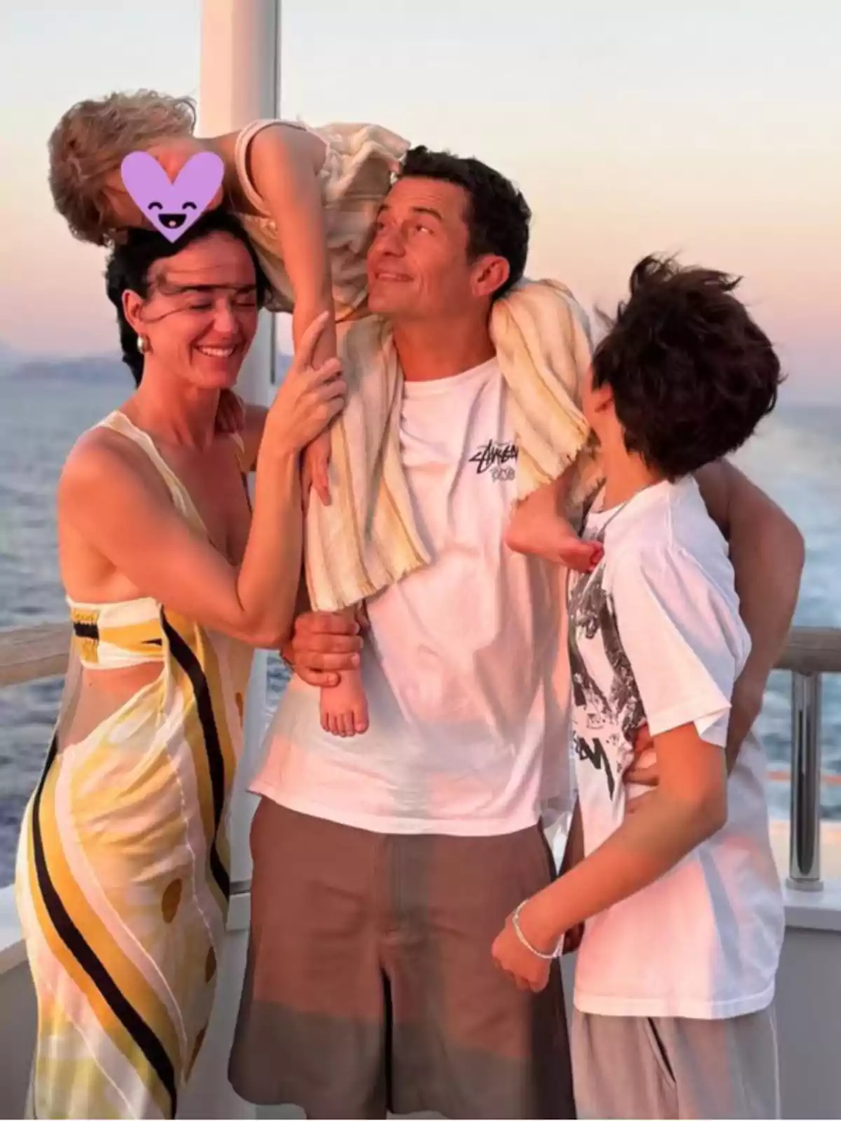 Smiling family enjoying a sunset on a boat while a small child is on the man's shoulders and their face is covered with a heart emoji. Smiling family enjoying a sunset on a boat while a small child is on the man's shoulders and their face is covered with a heart emoji.
